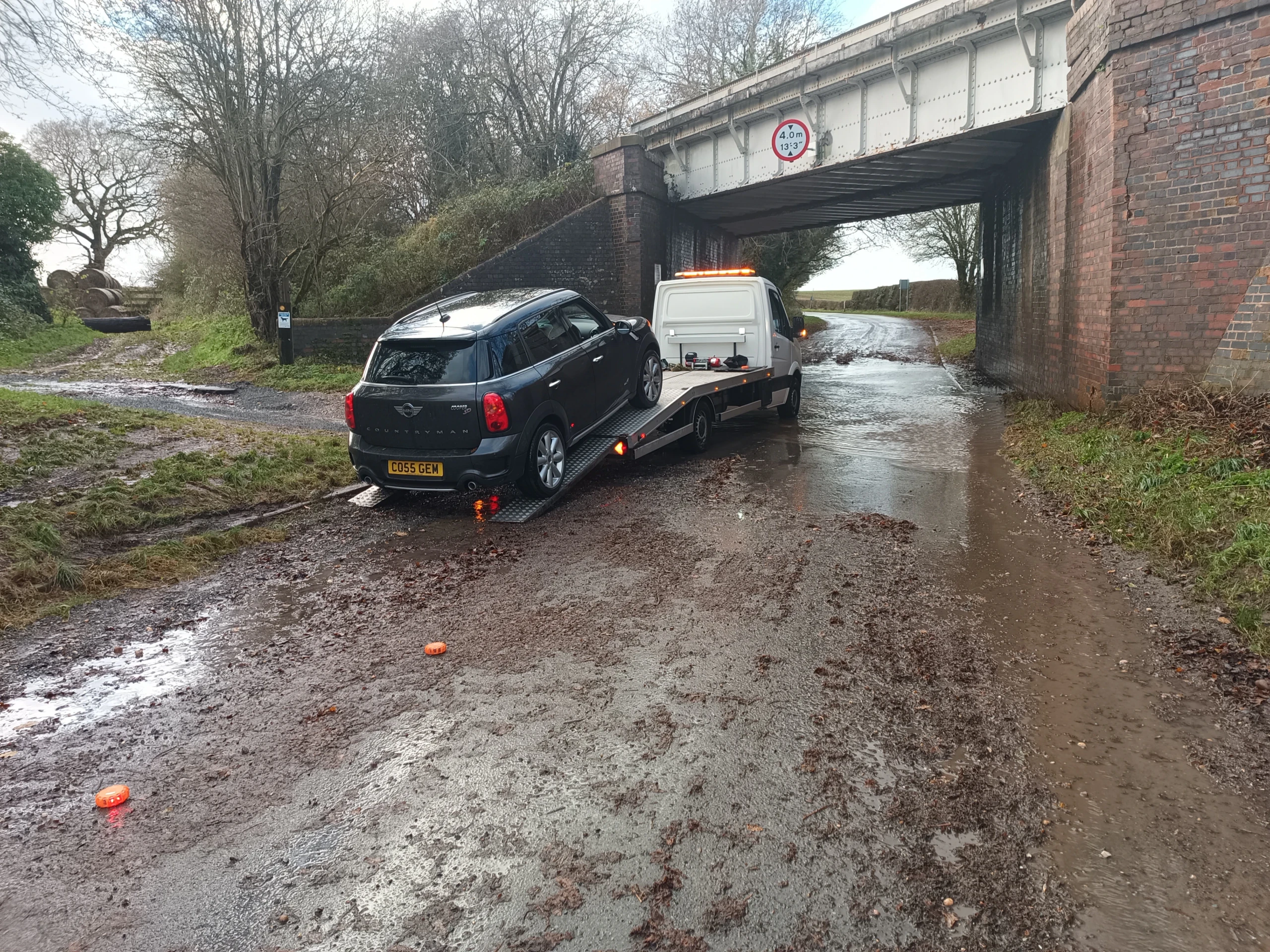 Car being winched out of a flooded road under a railway bridge
