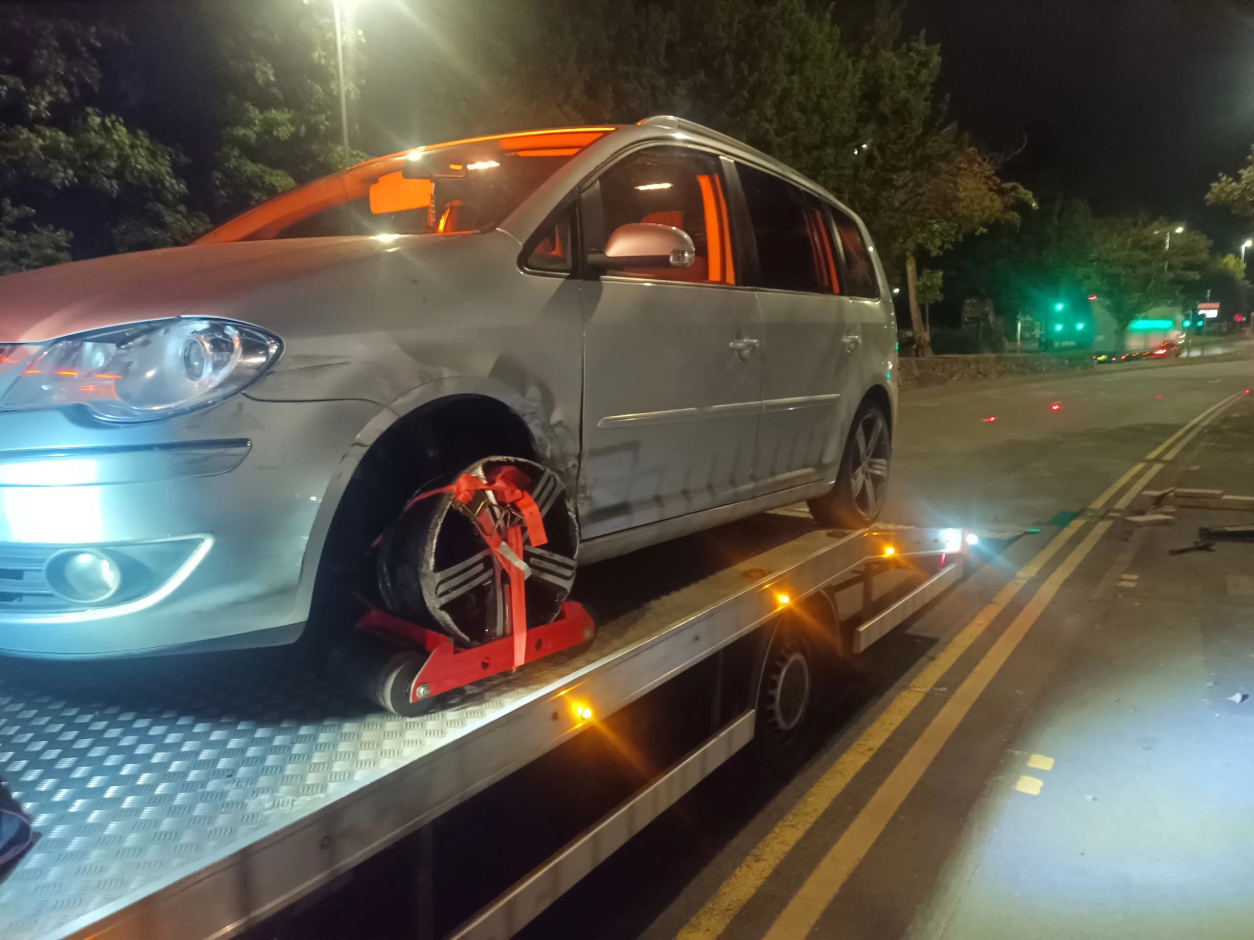 Car secured with wheel straps on a recovery truck at night