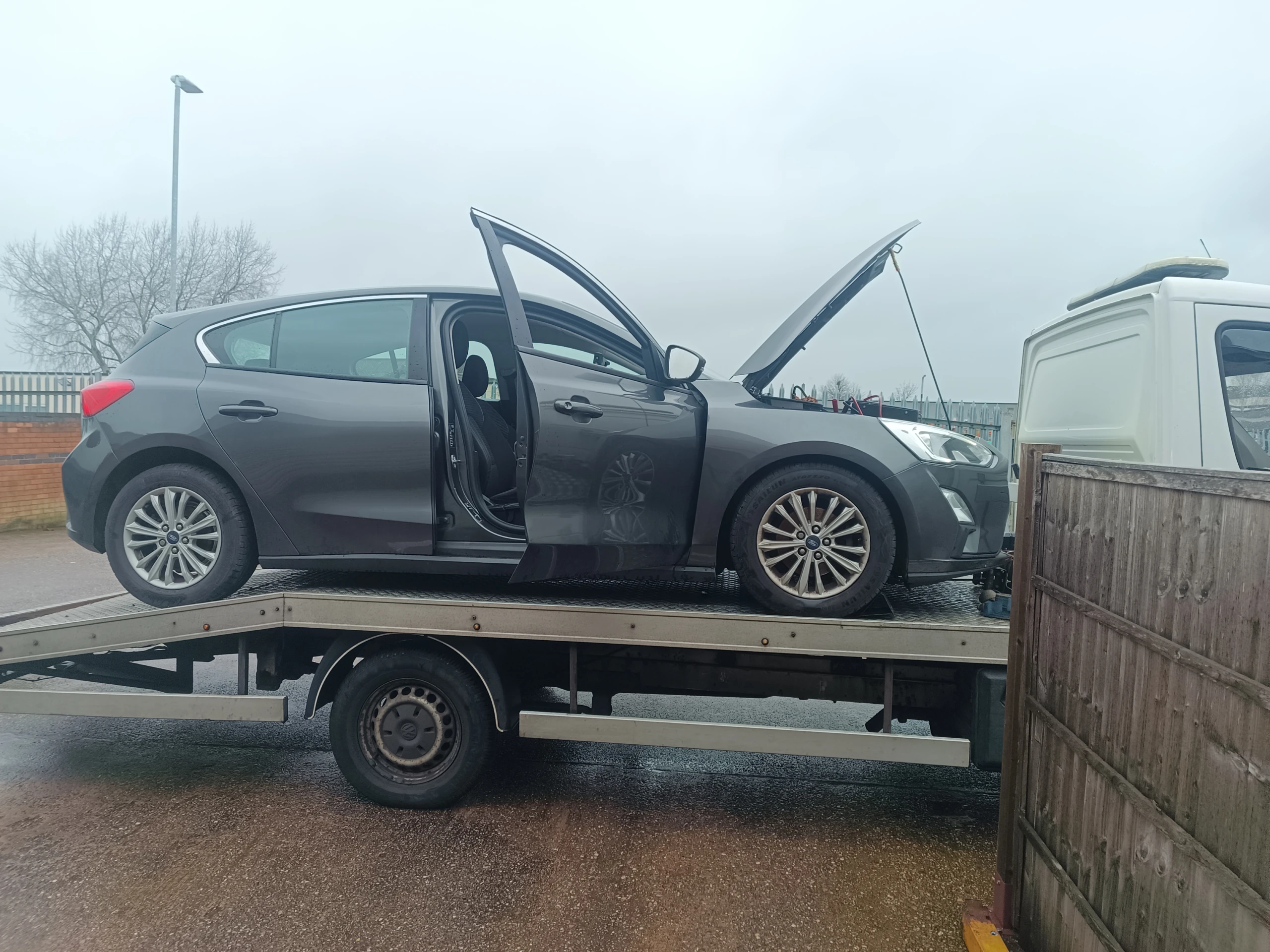 Broken-down car on a flatbed recovery truck with doors and bonnet open